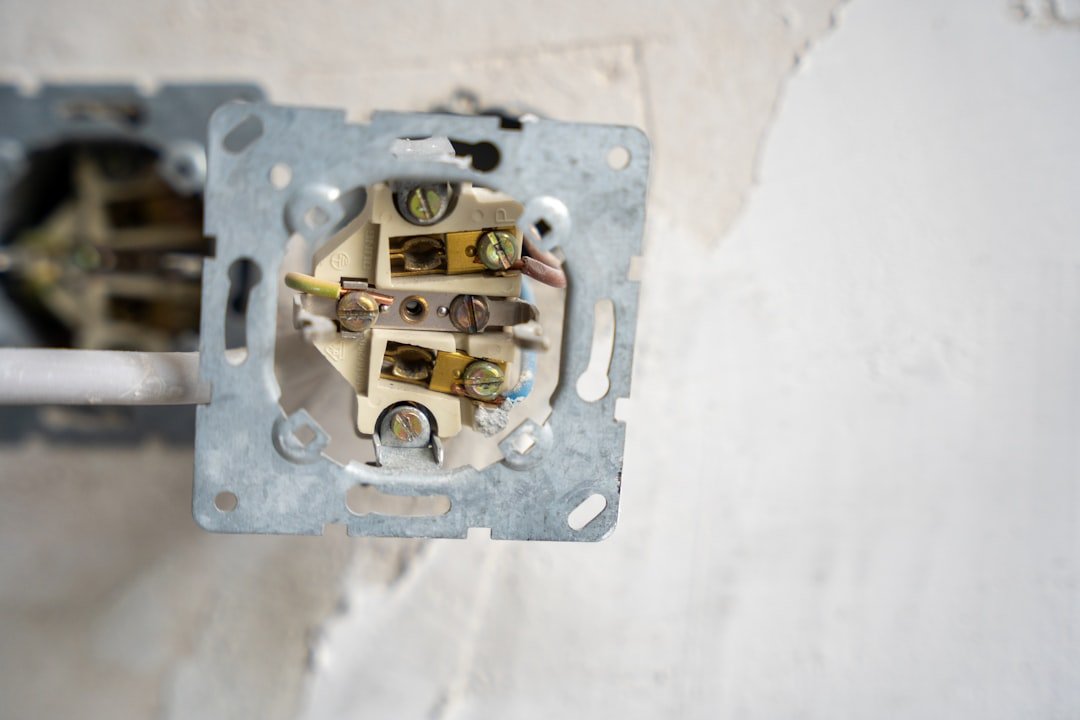 A detailed view of an in-progress electrical socket installation, revealing color-coded wiring and terminal screws set in a plaster wall. The image showcases the technical precision behind everyday power systems.