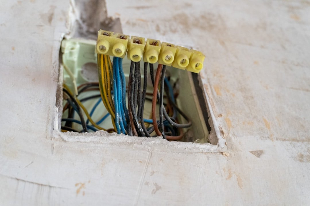 Services A close-up of an open electrical junction box set into a plaster wall, where neatly aligned colored wires are secured by a terminal block, revealing the hidden order behind interior wiring. The image conveys precision, safety, and the technical backbone of home renovation and electrical work.