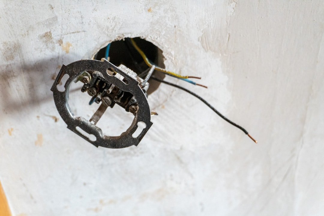 An exposed electrical wall socket emerges from a rough white plaster wall, with loose wires extending outward, capturing a raw moment of home renovation and unfinished construction. The minimal, industrial scene reflects maintenance, repair work, and the hidden infrastructure behind modern interiors.