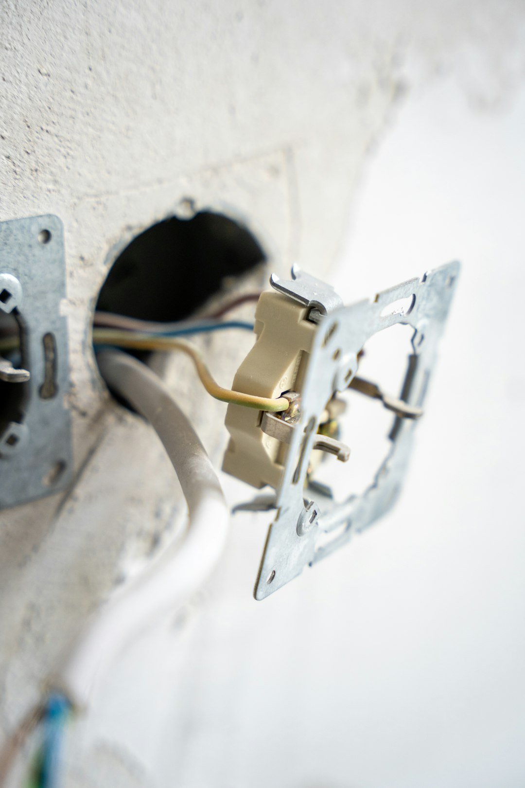 Services An exposed electrical wall socket in mid-installation, with visible wiring and mounting hardware set against a raw plaster wall. The image captures a hands-on moment in home renovation or electrical work.